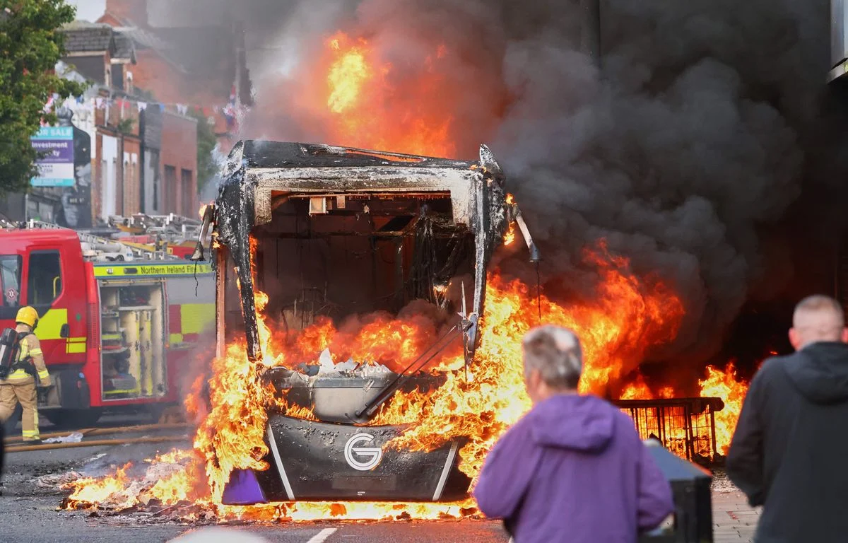 JUST IN: Knife attack, video, anti-immigrant violence… Update on the riots in Belfast 2 1200x768 des personnes regardent les pompiers arriver pour eteindre un vehicule incendie lors d une